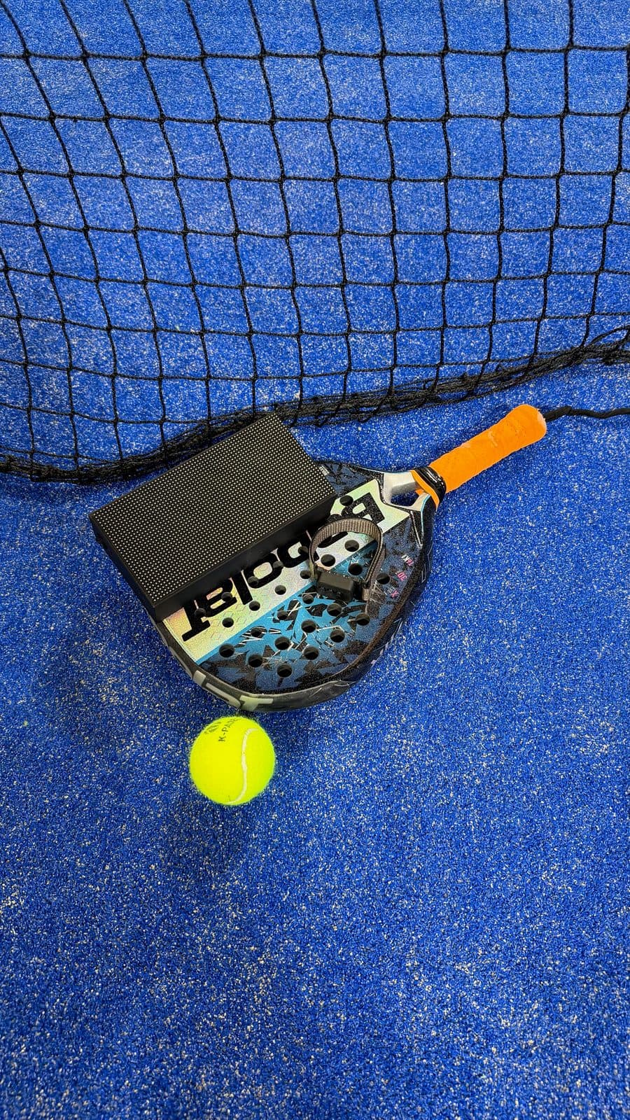 Le boîtier posé sur le gazon à côté d'une raquette de padel
